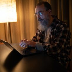 bearded man in plaid shirt with eyeglasses using laptop