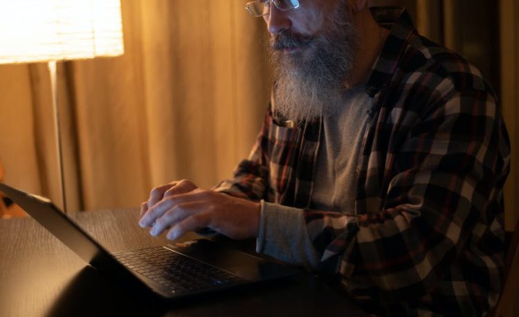bearded man in plaid shirt with eyeglasses using laptop