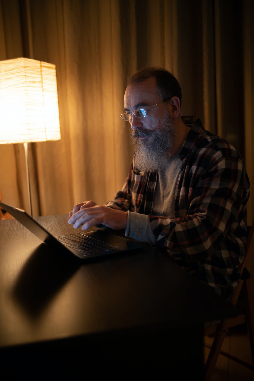 bearded man in plaid shirt with eyeglasses using laptop