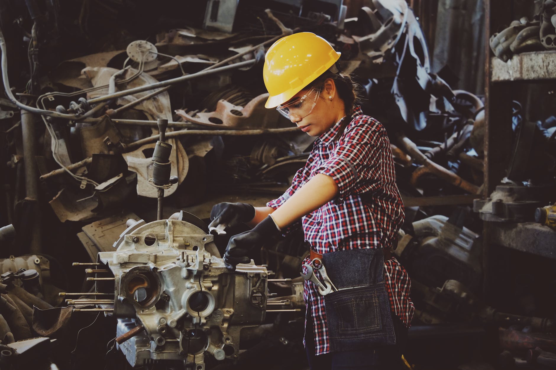 woman wears yellow hard hat holding vehicle part