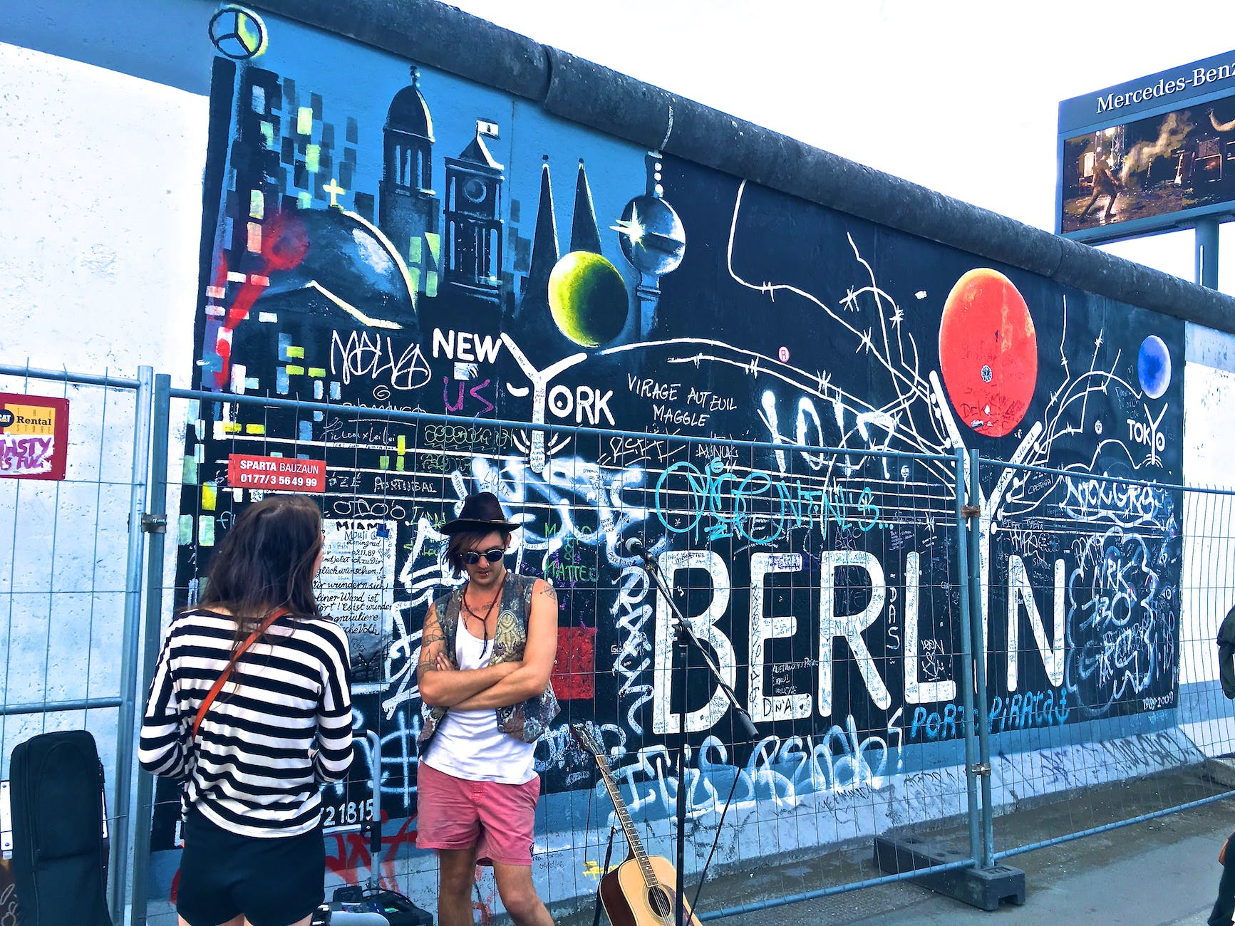 man wearing black waistcoat and white tank tops standing near a mural