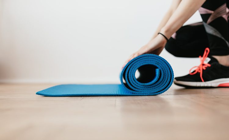 crop young sportswoman unfolding blue fitness mat