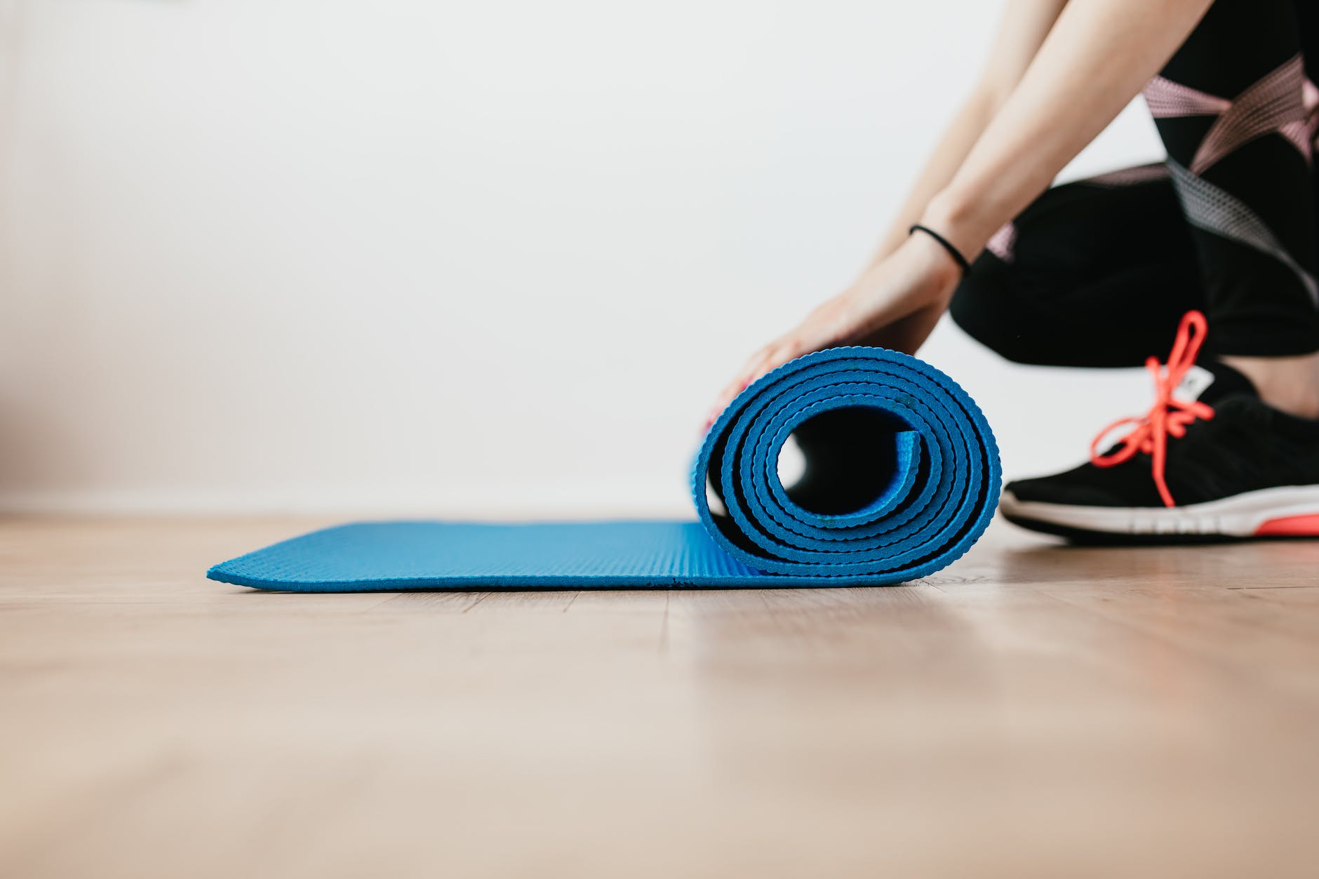 crop young sportswoman unfolding blue fitness mat