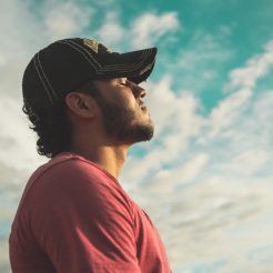 man wearing black cap with eyes closed under cloudy sky