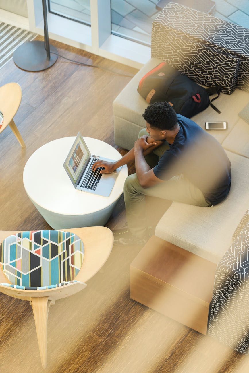 man using gray laptop while sitting on beige sofa