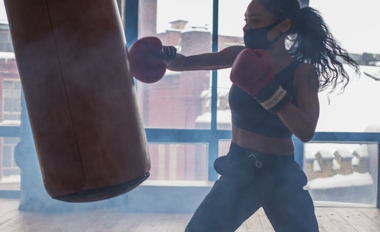 active black boxer punching heavy bag while exercising in gymnasium