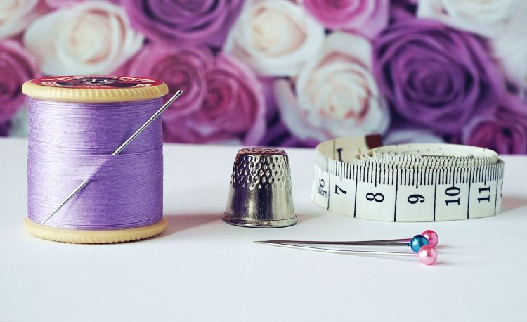 spool of purple thread near needle thimble and measuring tape