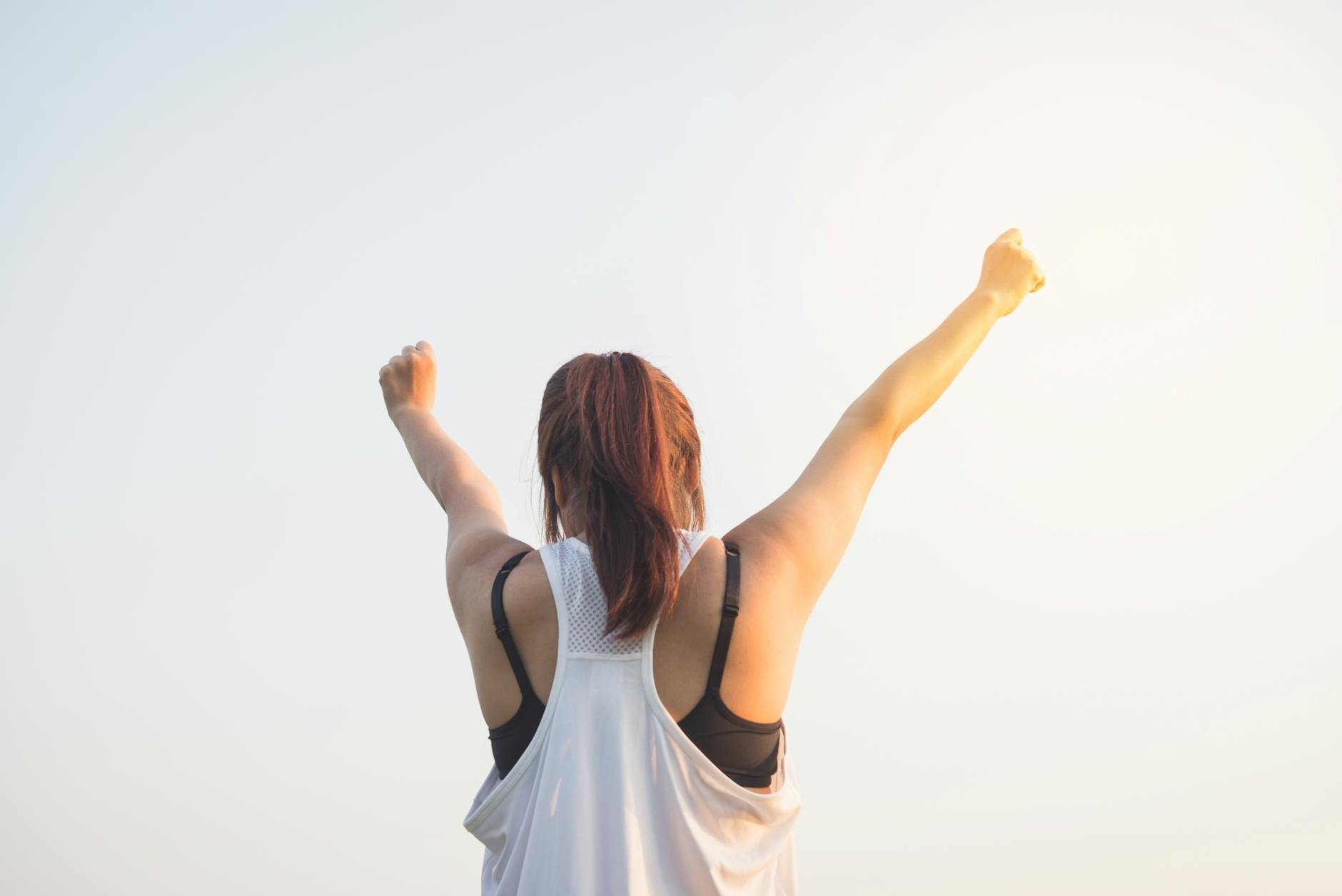 woman wearing black bra and white tank top raising both hands on top