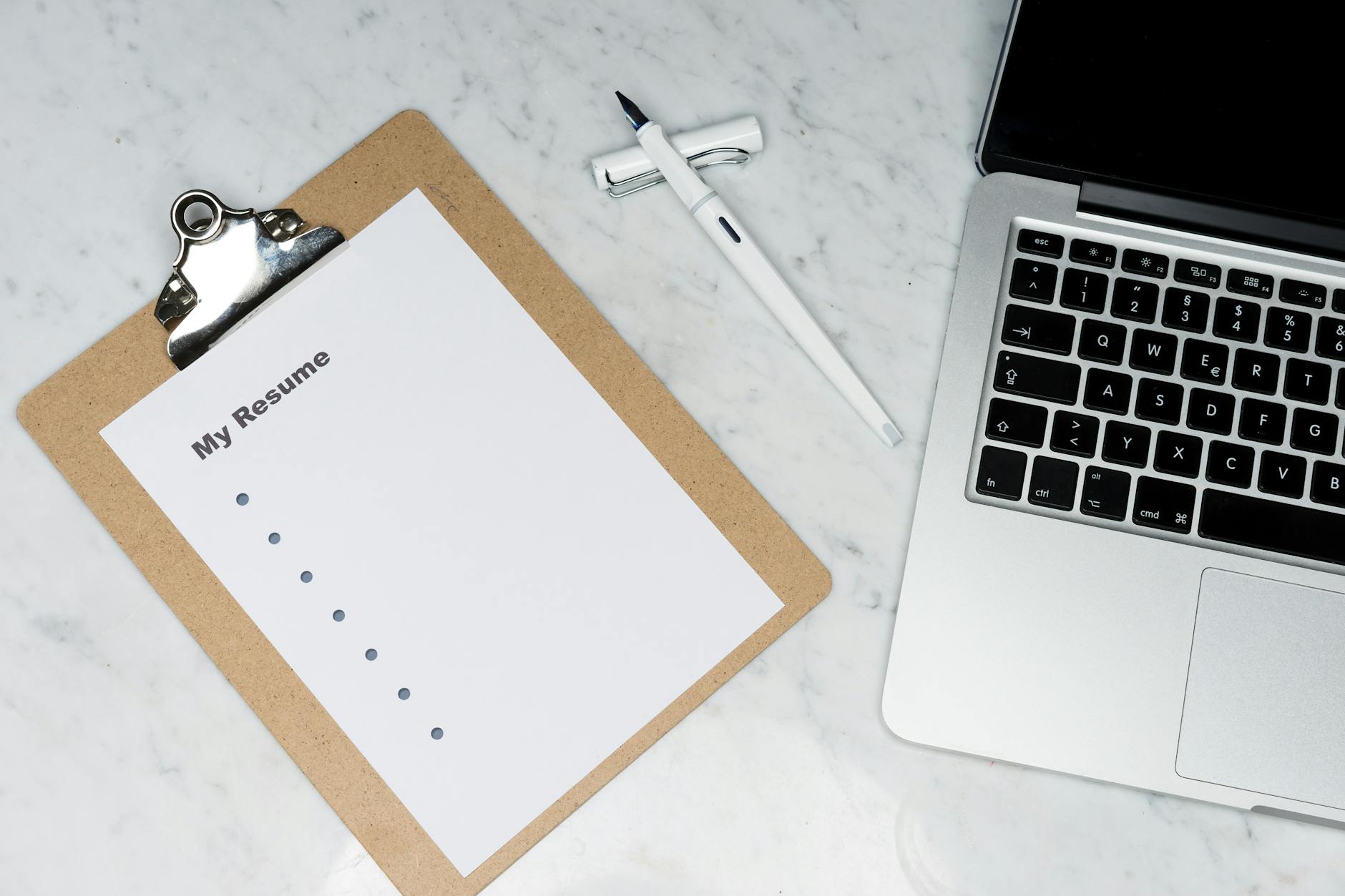 a clipboard near pen and laptop on a marble surface