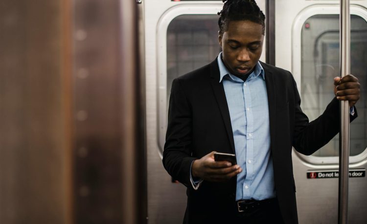 serious black office employee using smartphone on train