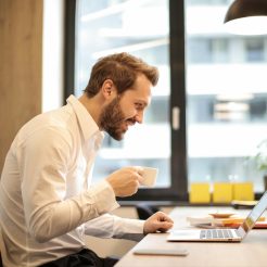 man holding teacup infront of laptop on top of table inside the room