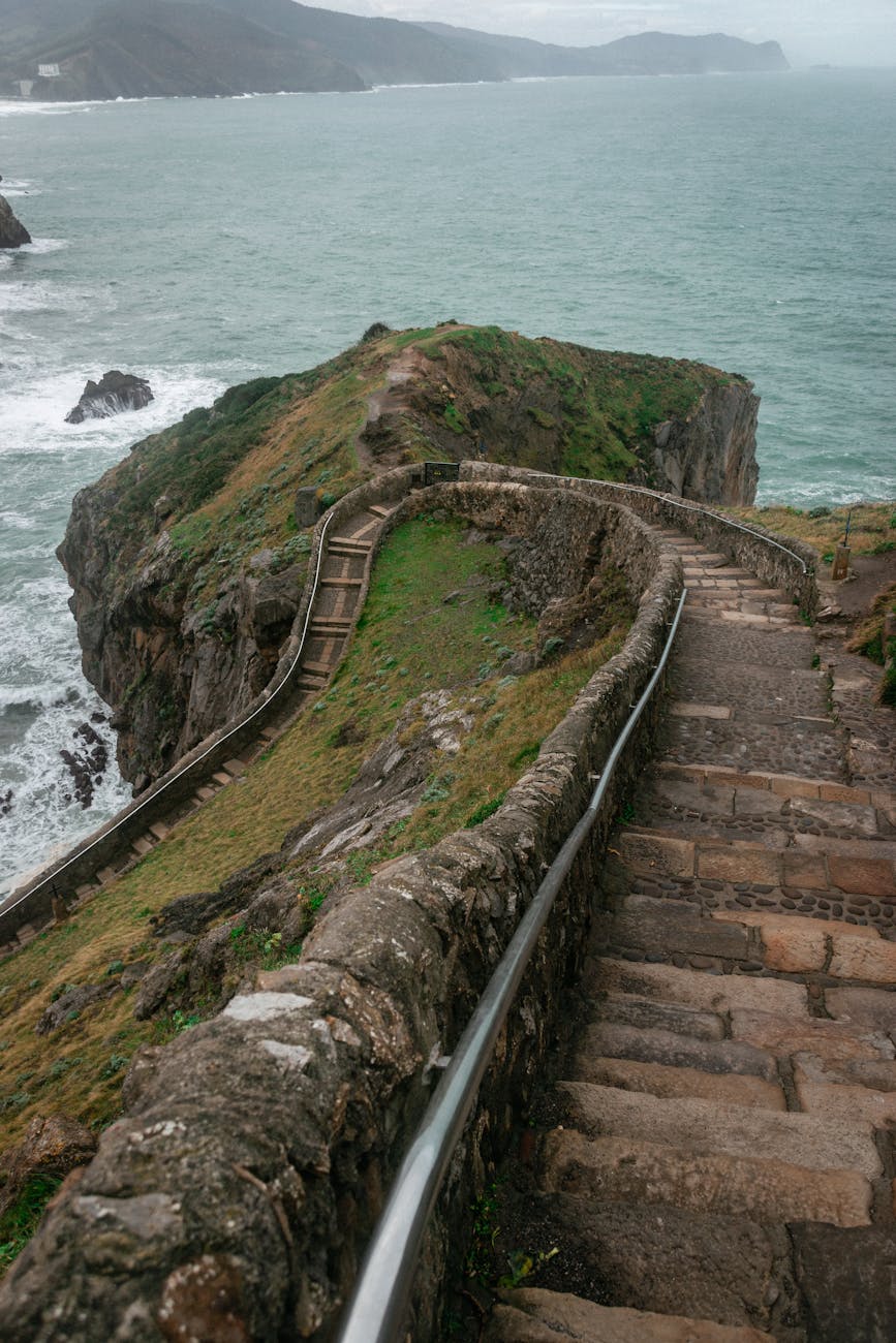 stone stairs leading through rocky cliff in wavy ocean against foggy sky