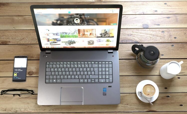 silver laptop next to coffe cup smartphone and glasses