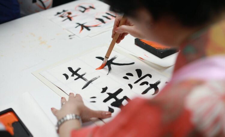 person holding brush drawing kanji script