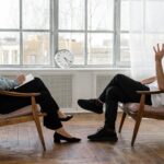 person in black pants and black shoes sitting on brown wooden chair