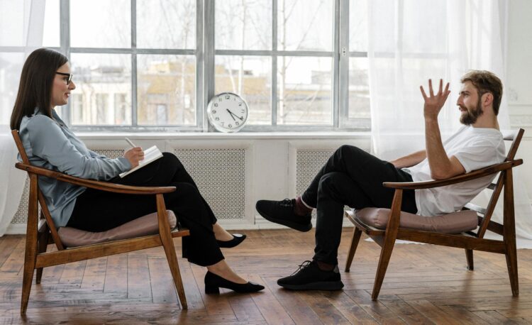 person in black pants and black shoes sitting on brown wooden chair