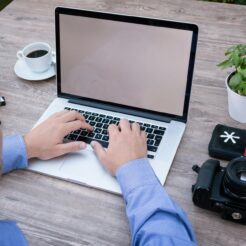 person using macbook pro beside dslr camera