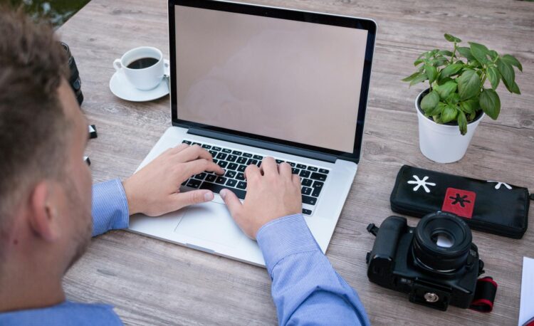 person using macbook pro beside dslr camera