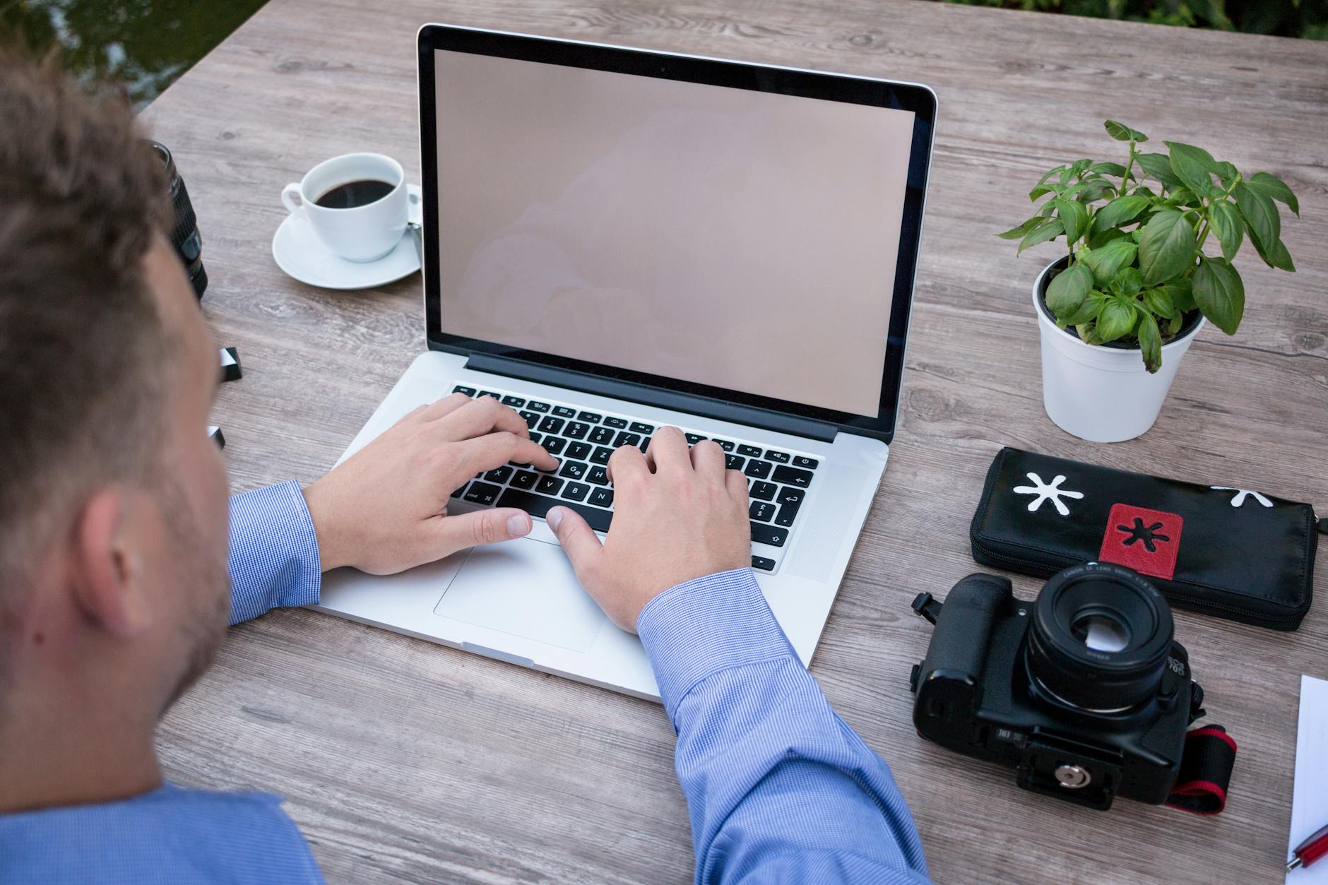 person using macbook pro beside dslr camera