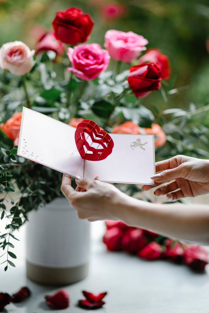 crop woman with valentine card near blooming flowers