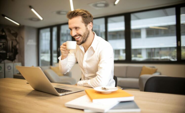 depth of field photo of man sitting on chair while holding cup in front of table