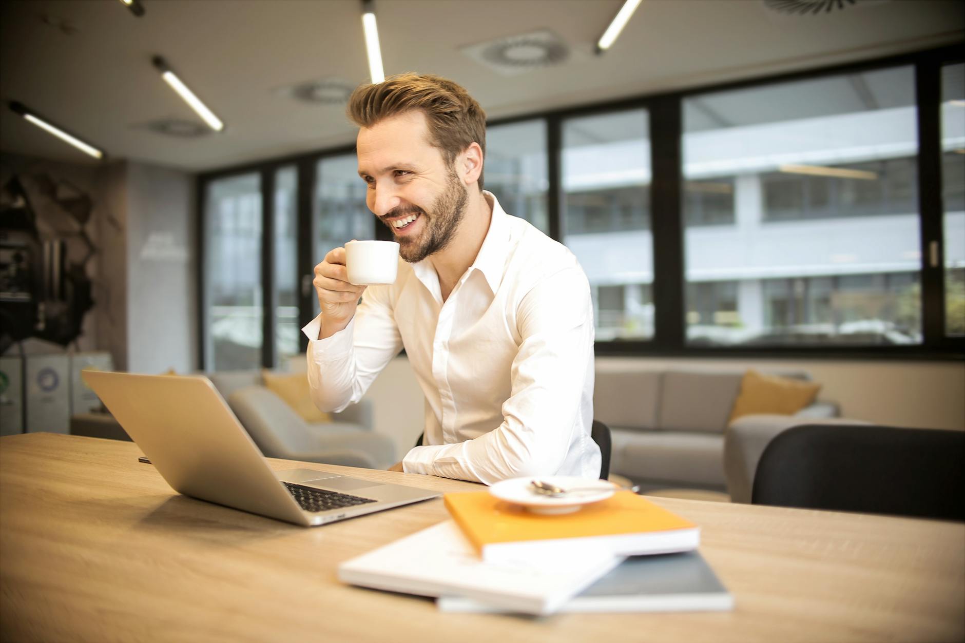 depth of field photo of man sitting on chair while holding cup in front of table